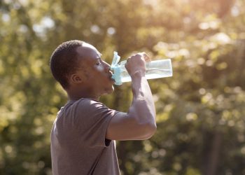 Overheated guy drinking water from bottle in park - Hometown Health Clinic